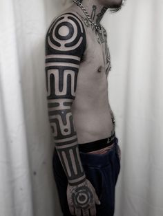 a man with tattoos and piercings on his arm standing in front of a curtain