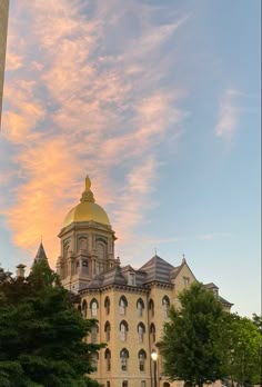 a large building with a golden dome on top and trees in the foreground at sunset