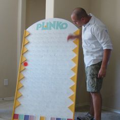 a man standing next to a giant sign that says plinko on it's side