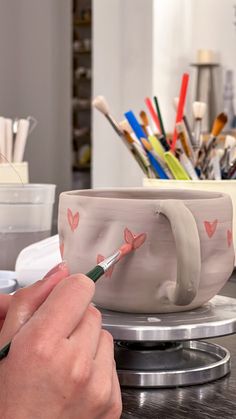 a person is painting a cup with paintbrushes on the table in front of them