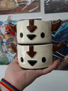 two ceramic mugs with brown and white designs on them, held in someone's hand