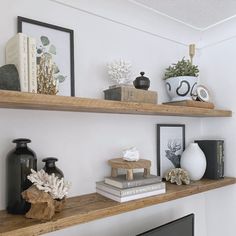 two wooden shelves with books and vases on them in a white walled room area