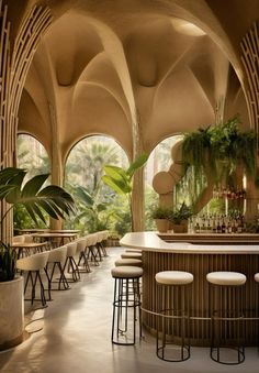 an indoor bar with stools and potted plants on the wall, in front of large arched windows