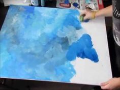 someone is painting blue and white clouds on a piece of paper with watercolors