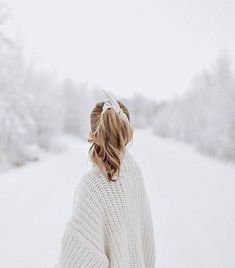 a woman standing in the snow with her back to the camera and wearing a white sweater