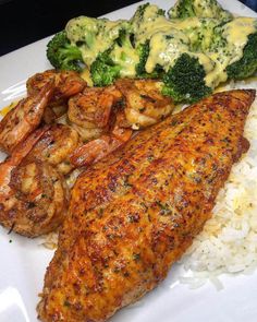 a white plate topped with chicken, shrimp and rice next to broccoli covered in sauce