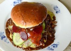 a hamburger covered in meat and vegetables on a white plate with blue floral design around it