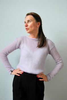 a woman standing with her hands on her hips wearing black pants and a light purple sweater