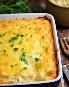 a casserole dish with cheese and green garnish in it on a wooden table