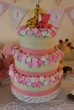 a three tiered cake is decorated with pink and green icing, flowers and giraffes