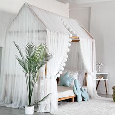 a bedroom with a canopy bed and white drapes on the walls, along with a potted plant