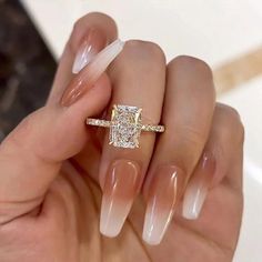 a woman's hand holding a gold ring with a diamond on it and some clear acrylic nails