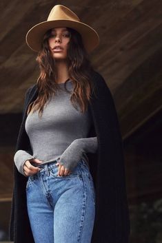 a woman in jeans and a hat is posing for the camera with her hand on her hip