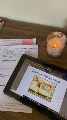 a tablet computer sitting on top of a wooden table next to a candle and some papers