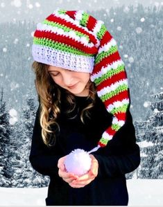 a woman holding a snowball in her hand while wearing a knitted hat and scarf