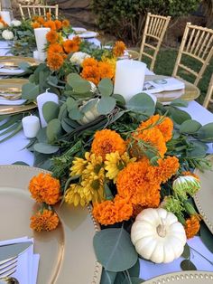 the table is set with orange and yellow flowers, greenery, candles and pumpkins