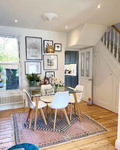 a dining room table with white chairs and pictures on the wall above it in front of stairs