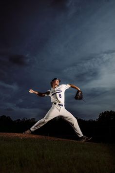 a baseball player pitching a ball on top of a lush green field under a cloudy sky