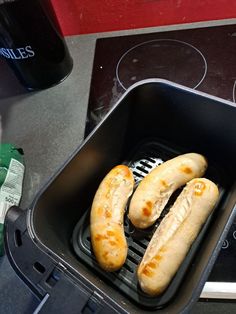 three hot dogs in a black container on top of a stove