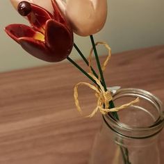 two fake flowers in a glass vase on a wooden table with string tied around the stems