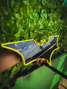 a person holding a mirror in front of green plants and leaves with the reflection of a bat on it