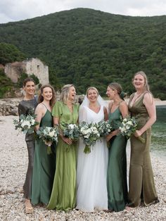 a group of women standing next to each other on top of a rocky beach with trees in the background