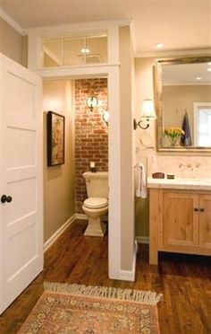 an open door leading to a bathroom with brick wall and wood floors, along with a rug on the floor