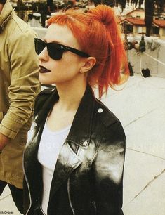 a woman with red hair and sunglasses walking next to a man in a leather jacket