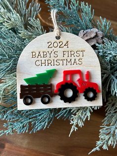 a baby's first christmas ornament hanging from a tree with two tractors