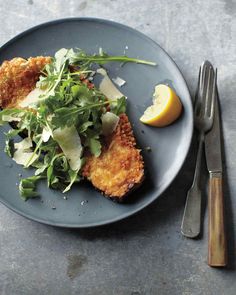 a blue plate topped with fried chicken next to a fork and lemon wedged salad