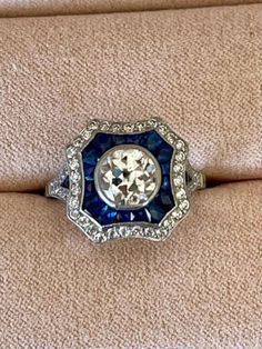 an antique ring with blue and white stones in the center on a beige fabric background