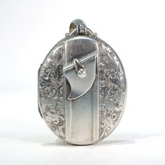 This extraordinary Victorian locket is a testament of everlasting love. Under the cover of a bed of flowers, fastened by a belt making an eternal loop, memories are worn close to your heart, preserved and protected forever. The Victorian Era was a time of symbolism and sentiment. A belt or buckle was a powerful symbol of love and loyalty, since it overlaps itself and fastens, creating a loop of eternity. In the past, people would place photos, small messages, even locks of hair inside, to keep loved ones always present. This Victorian Silver Locket with Belt Motif exhibits an illustration of a belt with a button fastener, surrounded by a gorgeous floral motif. Inside are two frames, with covers, lined with a peach-colored fabric. This lovely locket is a very wearable size, measuring 55.7 b Vintage Antique Silver Locket Necklace For Anniversary, Antique Silver Vintage Locket Necklace For Anniversary, Vintage White Gold Medallion Locket Necklace, Vintage Engraved White Gold Locket Necklace, Vintage White Gold Locket Necklace As A Gift, Vintage White Gold Locket Necklace Gift, Vintage White Gold Jewelry With Engraving Option, Vintage White Gold Locket Necklace For Gift, Vintage White Gold Locket Necklace For Anniversary