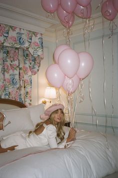 a woman laying in bed with pink balloons