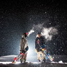 two snowboarders standing in the snow at night