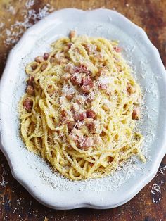 a white plate topped with pasta covered in sauce and meat toppings on top of a wooden table