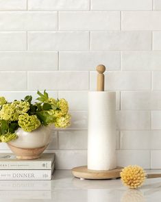 a white vase filled with yellow flowers on top of a counter next to a stack of books