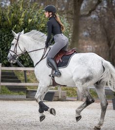 a woman riding on the back of a white horse in an enclosed area with trees