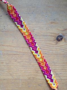 a close up of a colorful bracelet on a wooden table next to an orange, yellow and pink bead cord