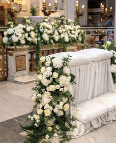 a white bench covered in flowers and greenery next to a fire place filled with candles