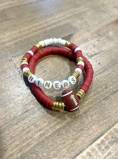 two red and white beaded bracelets with football charms on top of a wooden table