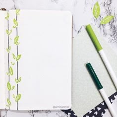 an open notebook with green leaves on it next to a pen and paper clippings