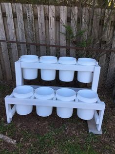 several white plastic buckets are stacked on a shelf in front of a wooden fence