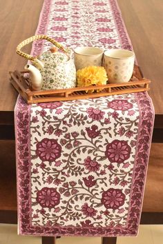 a table runner with cups and teapots on it, sitting on top of a wooden table