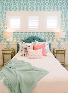 a white bed topped with lots of pillows next to two nightstands and a window