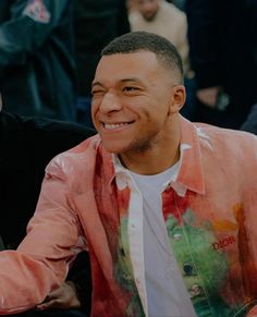 a man sitting in front of a crowd wearing a pink jacket and white t - shirt