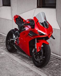 a red motorcycle parked on the side of a road next to a building with windows