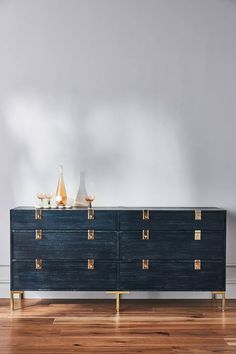 a large blue dresser with gold handles on it in a white walled room next to a wooden floor