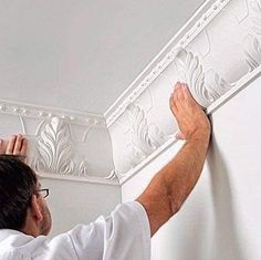 a man is working on the ceiling in his home with white paint and decorative molding