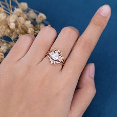 a woman's hand with a ring on it and flowers in the background,