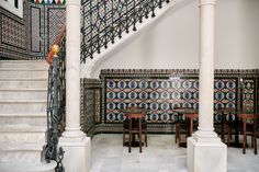 an ornately decorated staircase and table in a room with patterned walls, white marble floors and black iron handrails